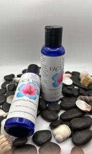 Two Face cleanser bottles with floral designs on a bed of pebbles and shells.