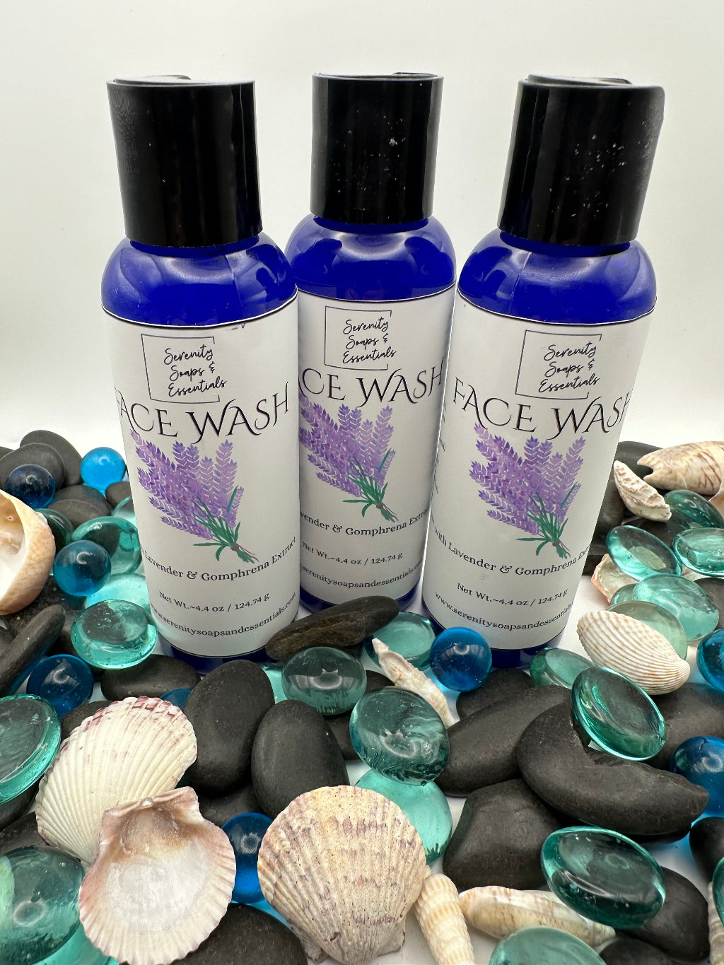 Three bottles of lavender face wash on pebbles and shells