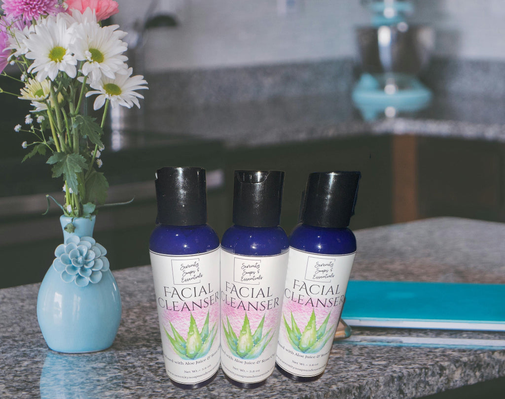 Three bottles of facial cleanser on a countertop with flowers and a notebook in the background.