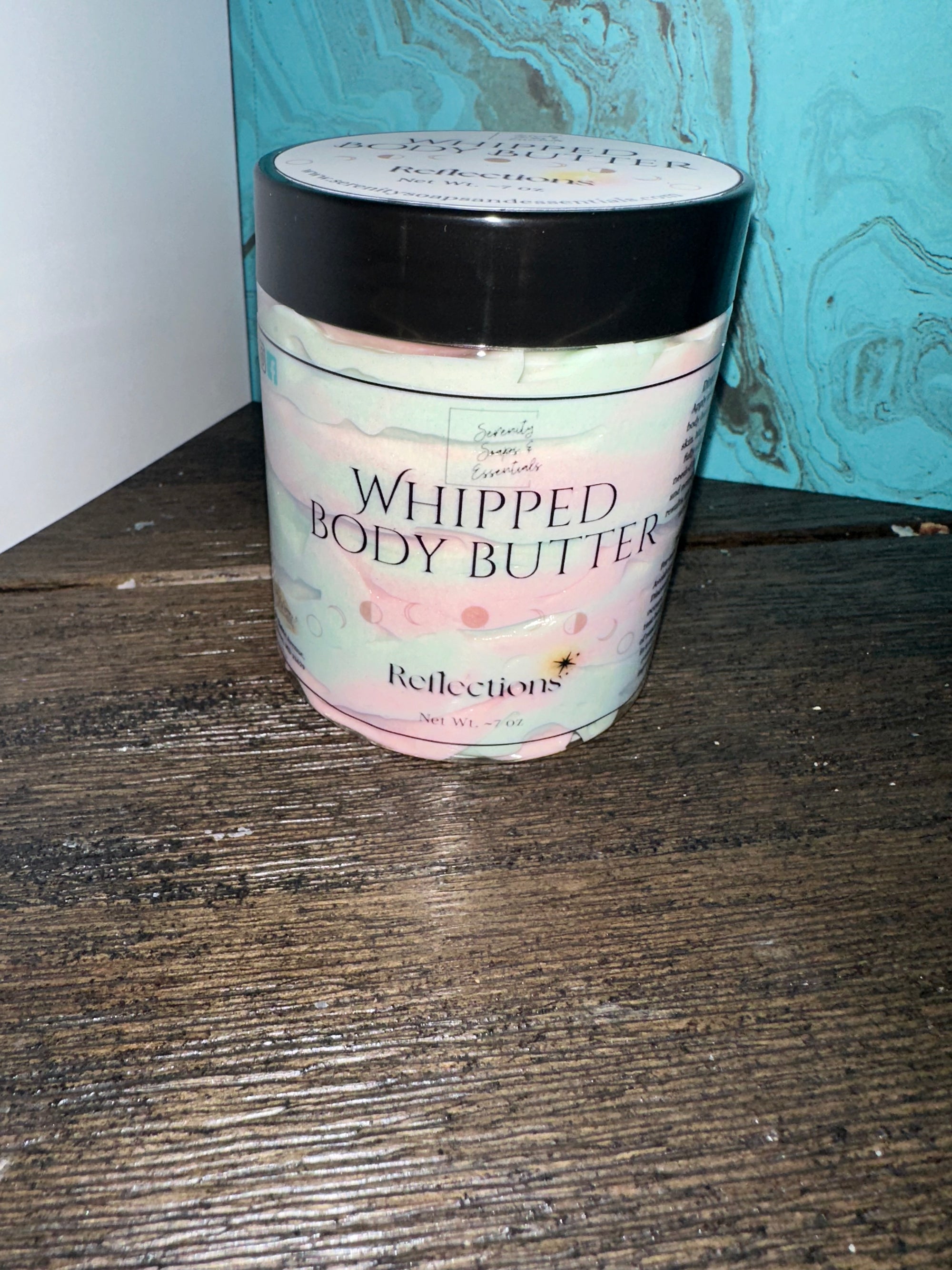 Jar of whipped body butter named “Reflections” on wooden table