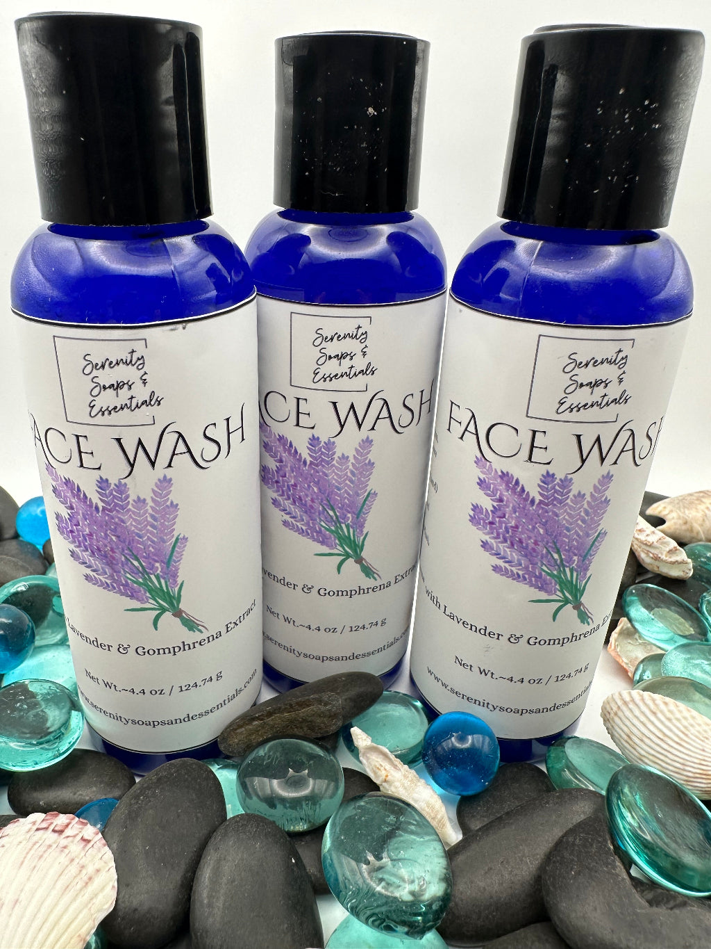 Three bottles of Lavender Face Wash with black caps on a background of stones and seashells.