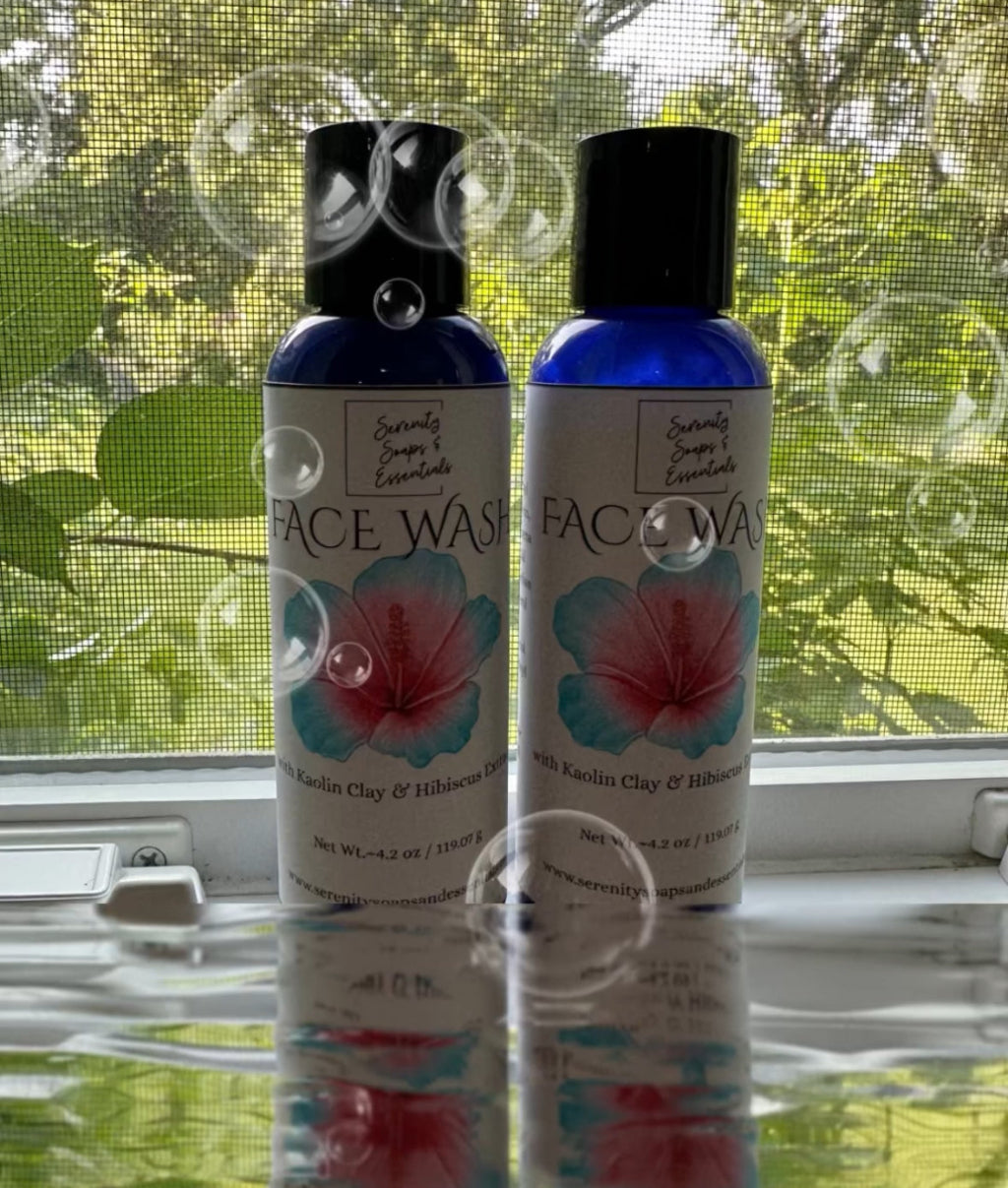 Two bottles of face wash on a reflective surface with a window and greenery in the background.
