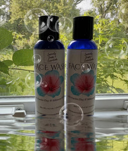 Two bottles of face wash on a reflective surface with a window and greenery in the background.
