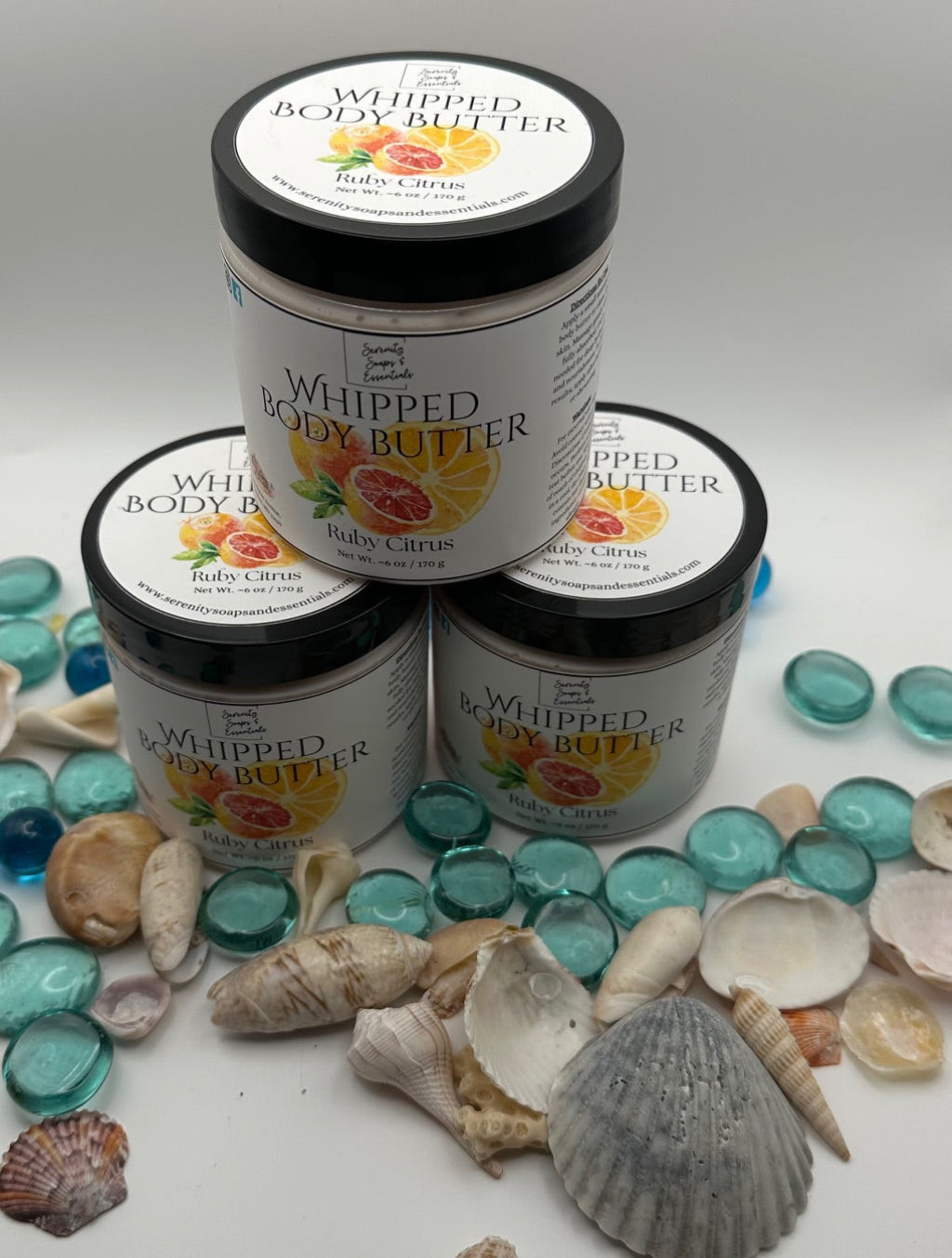 Three jars of whipped body butter with a decorative background of seashells and glass beads.