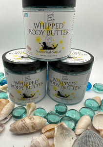 Three jars of 'Whipped Body Butter' by Nocturnal Noctar on a white background with seashells and blue stones.