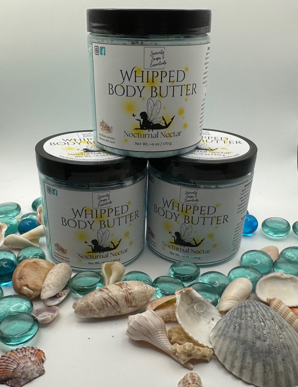 Three jars of 'Whipped Body Butter' with 'Nocturnal Nectar' branding on a surface with seashells and glass beads.