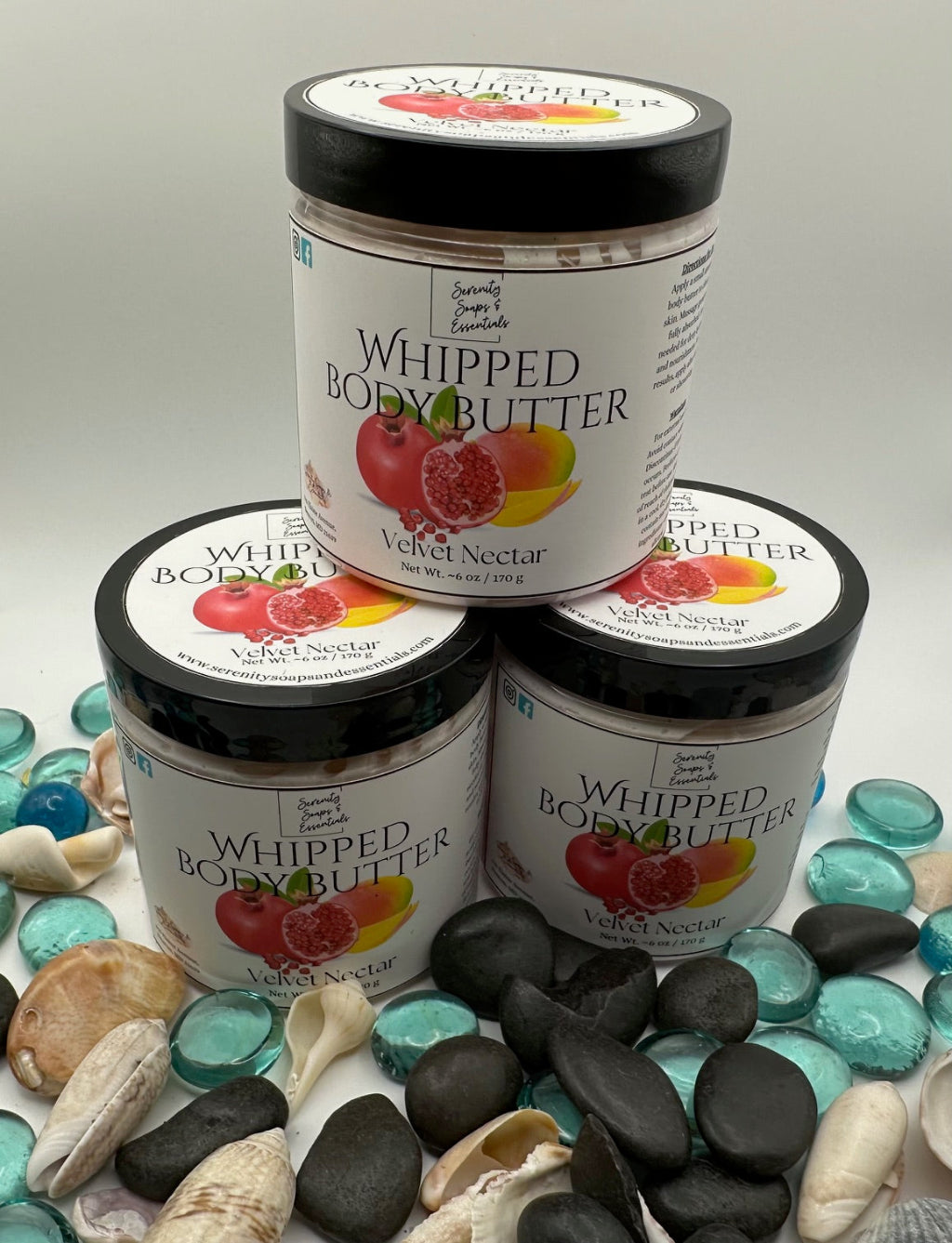 Four jars of Whipped Body Butter stacked on a surface with pebbles and stones.
