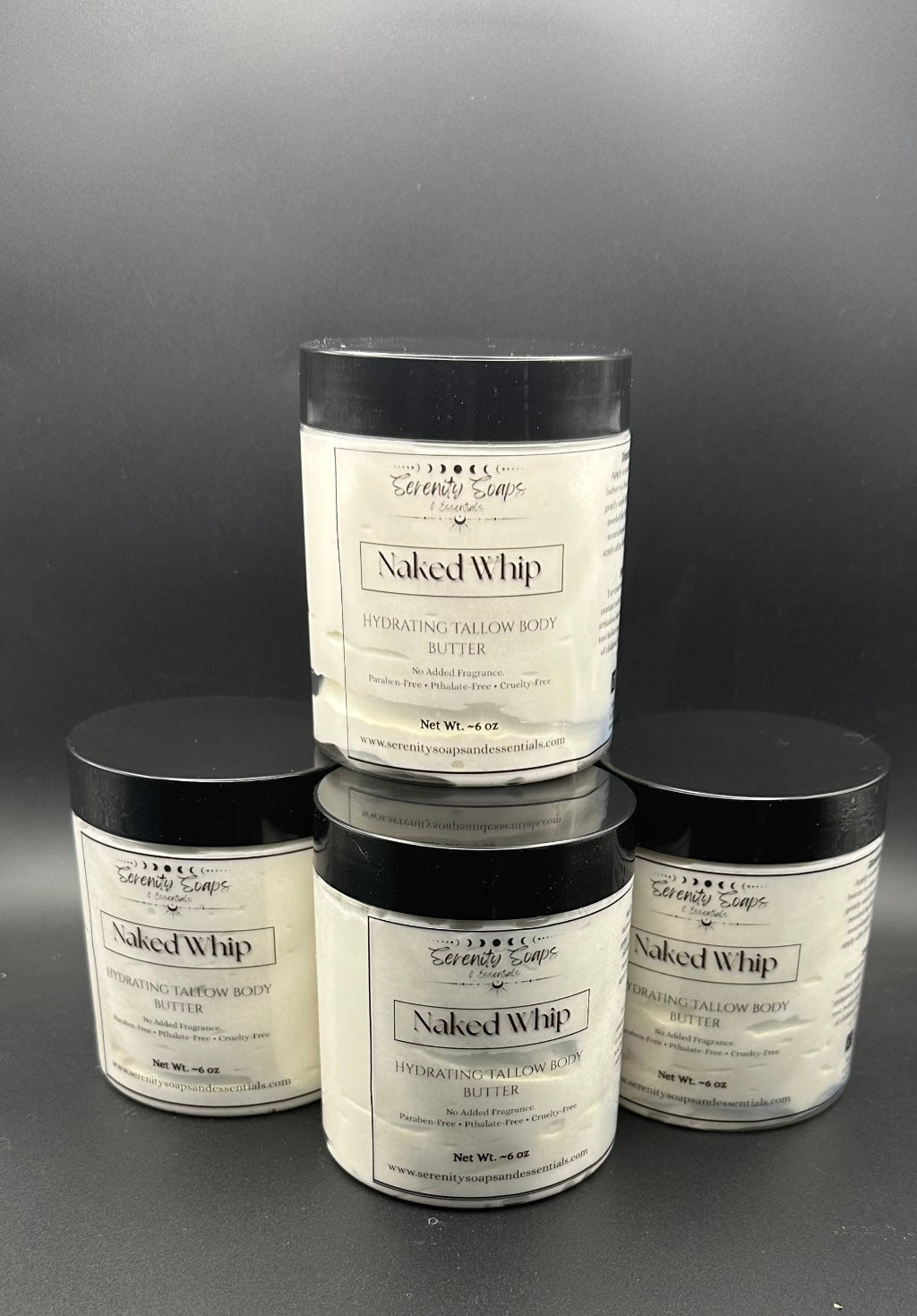 Four containers of Naked Whip body butter stacked on a dark background